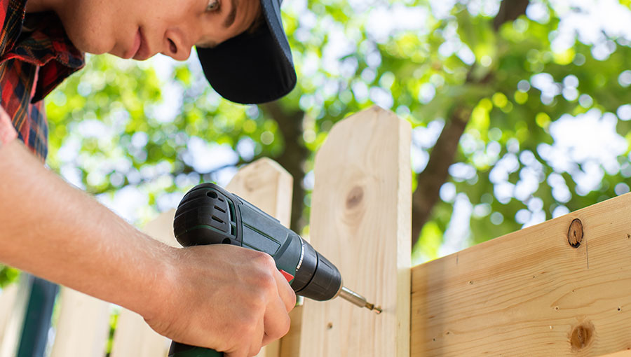 Young handsome man using electric cordless drill on wooden fence